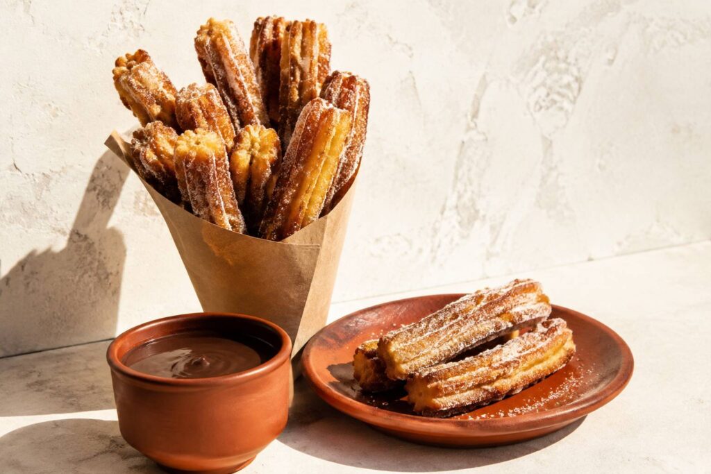 Churros dorés saupoudrés de sucre dans un cornet avec chocolat chaud