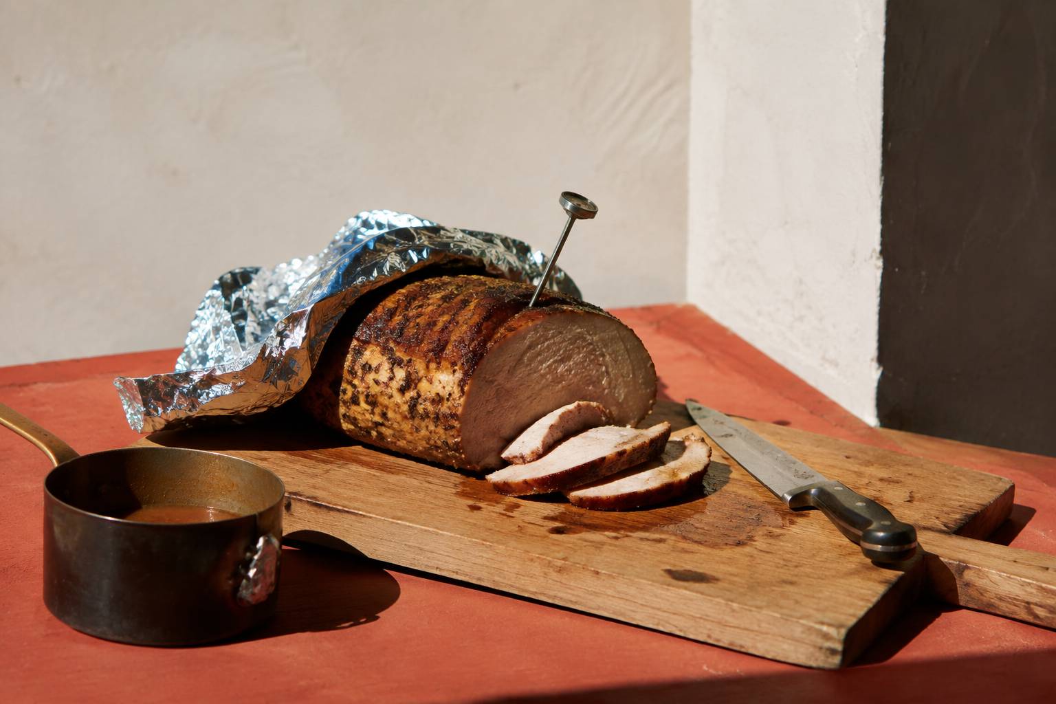 Rôti de porc au repos sur une planche avec thermomètre de cuisson et couteau à découper